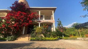 A two-story building with a balcony, surrounded by a garden with red flowers and various plants.