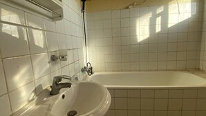 A bathroom with a sink and bathtub, tiled walls, and a showerhead.