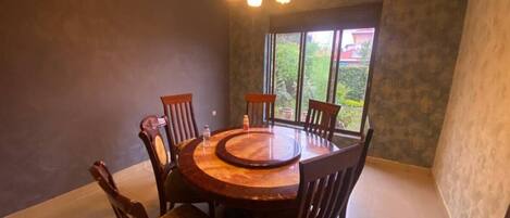 Un comedor con una mesa redonda de madera, seis sillas y una lámpara de araña.