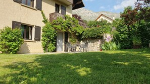 Un bâtiment doté d’une façade en pierre, d’un balcon avec des balustrades en bois et d’un petit patio aménagé avec une table et des chaises.