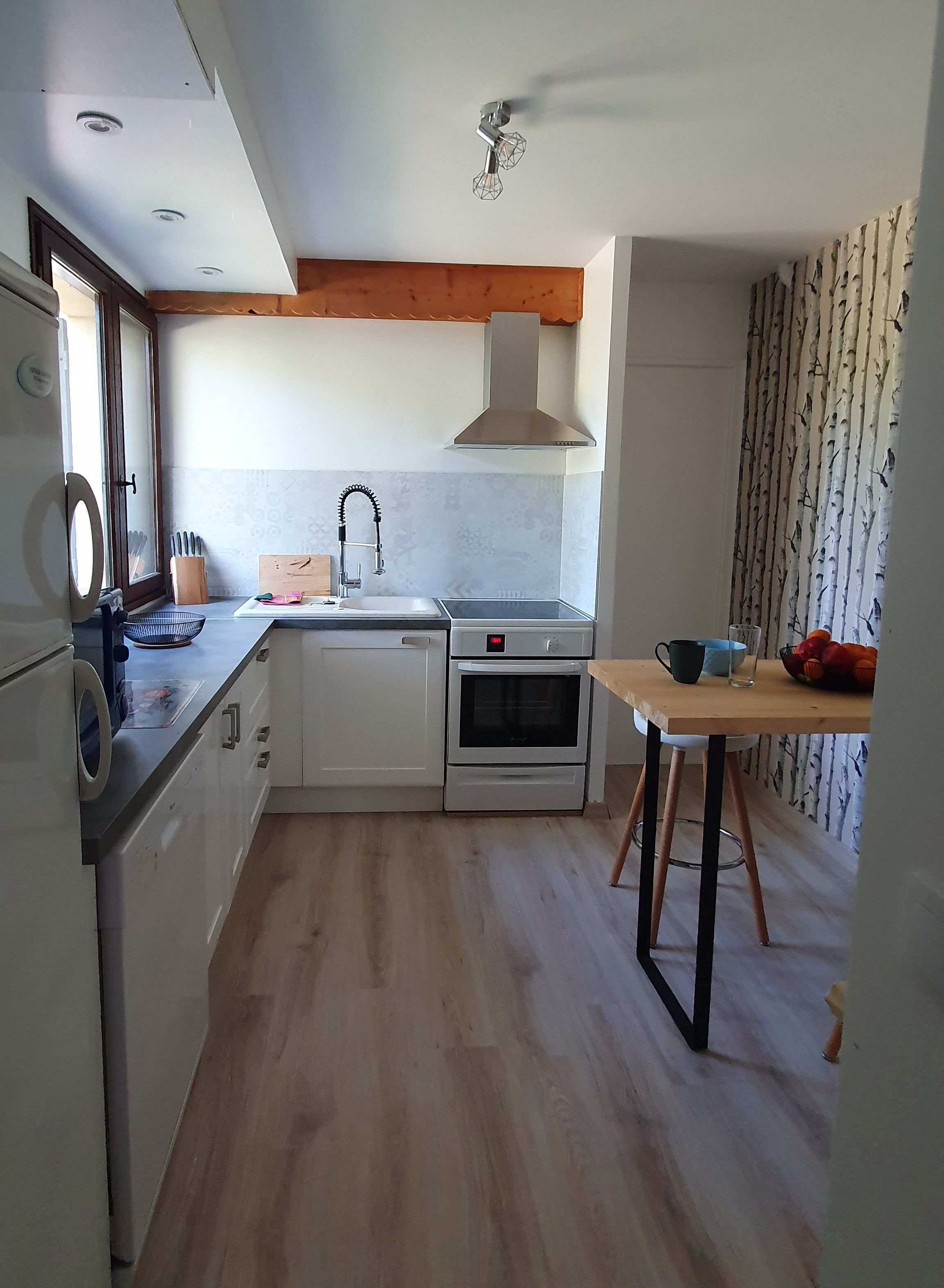 Una cocina compacta con armarios blancos, horno empotrado, un lavamanos y una mesa de comedor de madera.