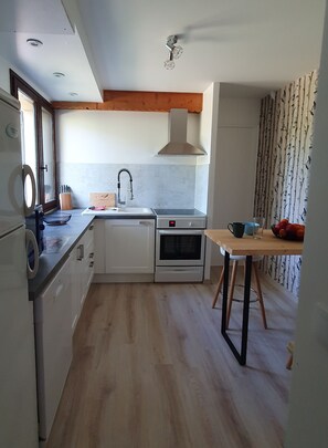 A compact kitchen with white cabinets, a built-in oven, a sink, and a wooden dining table. - Comfortable T2 Vacation Home Near a Resort (Dévoluy)