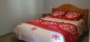 Un lit avec une couvre-lit à motifs rouges et blancs et des coussins assortis, une tête de lit en bois et une petite table de chevet.
