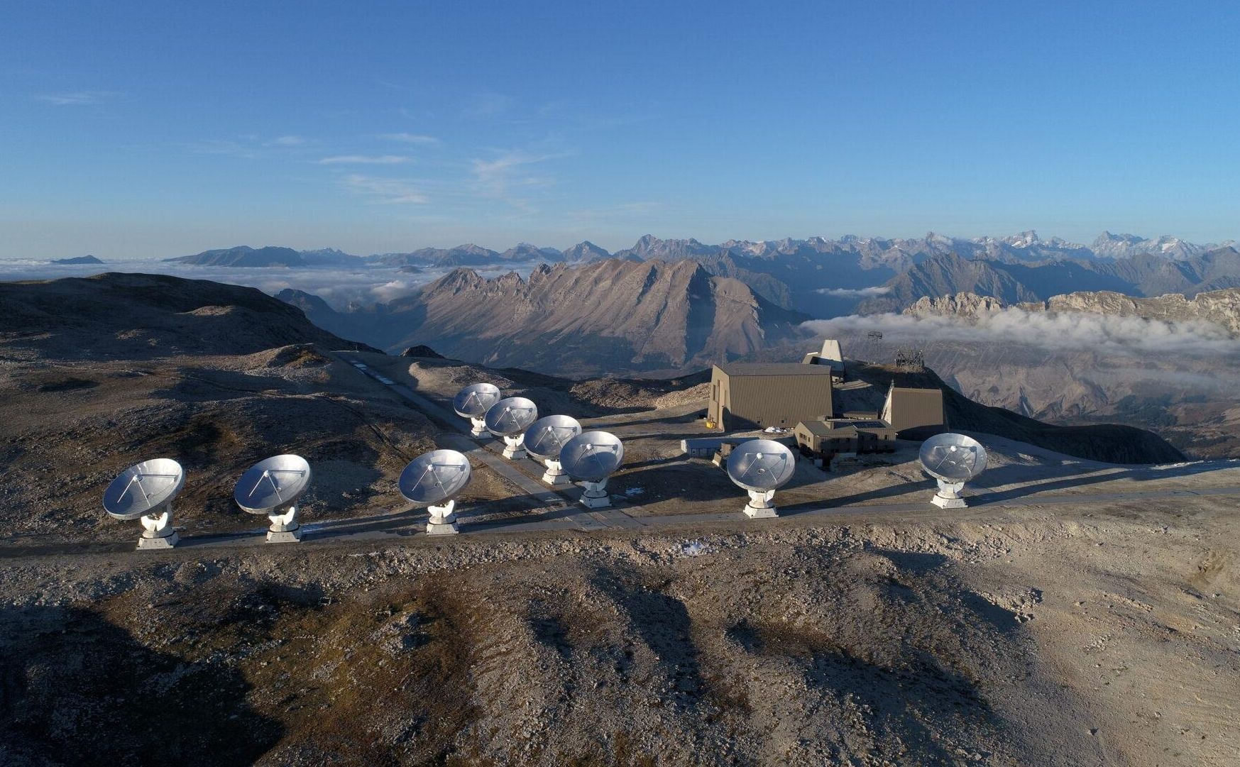 Et afsides beliggende observatorium med flere parabolantenner, omgivet af bjerrelandskab og klare himle.