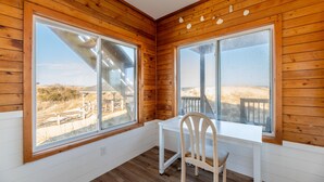 Una habitación de esquina con paredes de madera, ventanas amplias, un escritorio blanco y una silla.