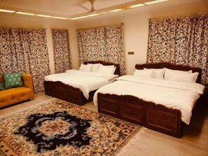 A hotel room with two wooden beds, a yellow sofa, patterned curtains, and a decorative rug. - New Zamrood Holiday Home  (Srinagar)