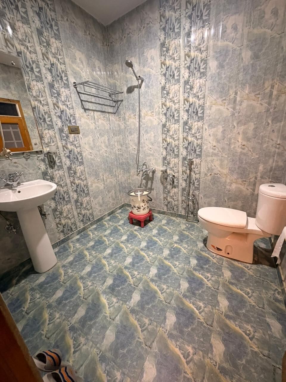 A bathroom with a marble floor, a sink, a toilet, and a shower.