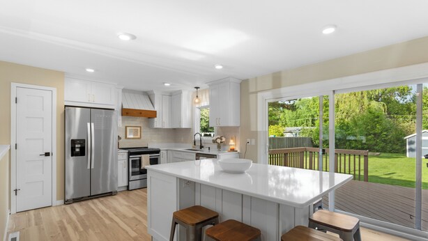 A modern kitchen with a large island, stainless steel appliances, and a view of the backyard through large sliding glass doors.