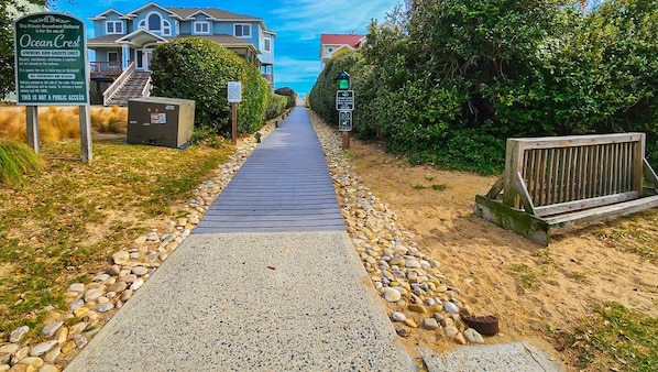 Een privépad aan zee met een houten vlonder, omgeven door huizen en weelderige begroeiing.