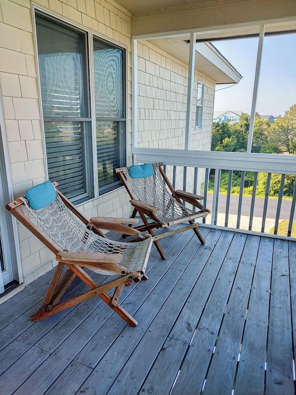 Een houten terras met twee rieten ligstoelen en een witte balustrade.