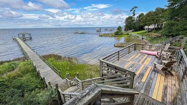 Un muelle de madera que se adentra en una masa de agua tranquila, con una zona de cubierta que incluye barandillas y asientos.