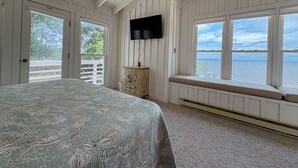 Un dormitorio con cama, cómoda, televisor y ventana con vista al agua.