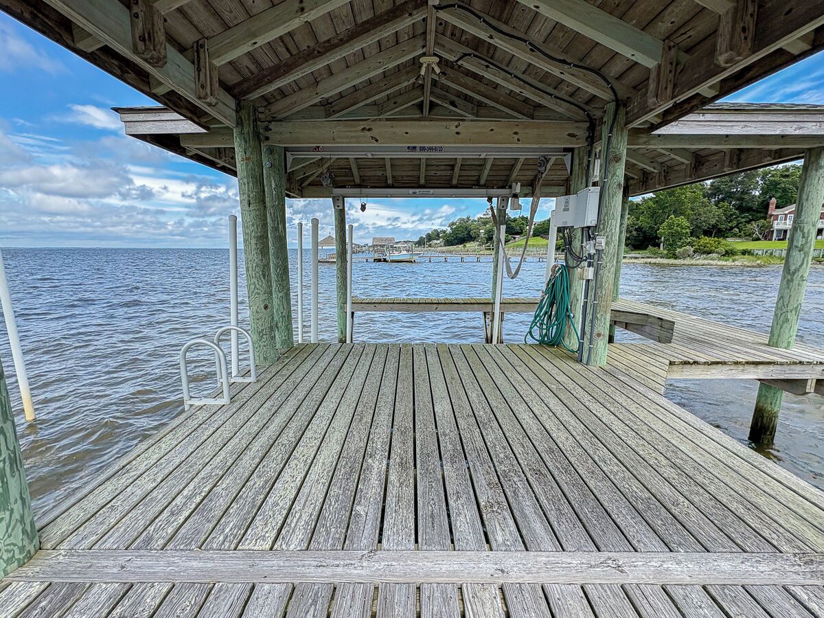 A wooden pier with a covered area, metal railings, and a view of the water and distant land.
