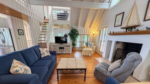 Un salón espacioso con un sofá azul, un sillón gris, una mesa de centro de madera y una chimenea.