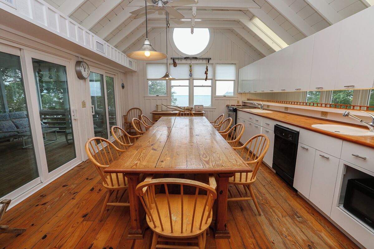 A spacious kitchen with a large wooden table and chairs, white cabinets, and a view of the outdoors.