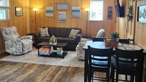 Un salon chaleureux avec un plancher en bois, un canapé, une table à manger avec des chaises et un ventilateur de plafond.