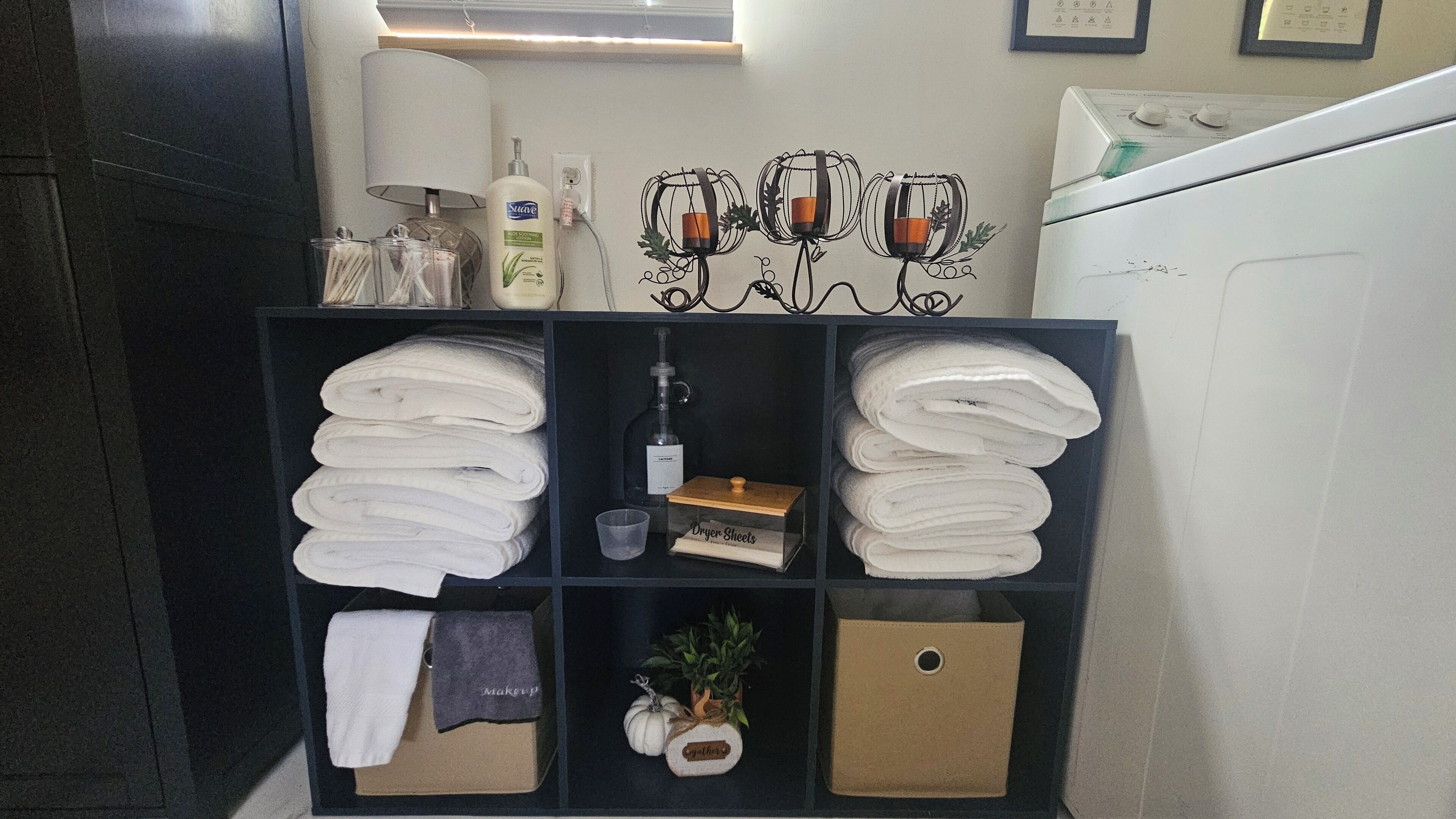 A neatly organized storage unit with folded towels, a bottle of lotion, and a small plant.