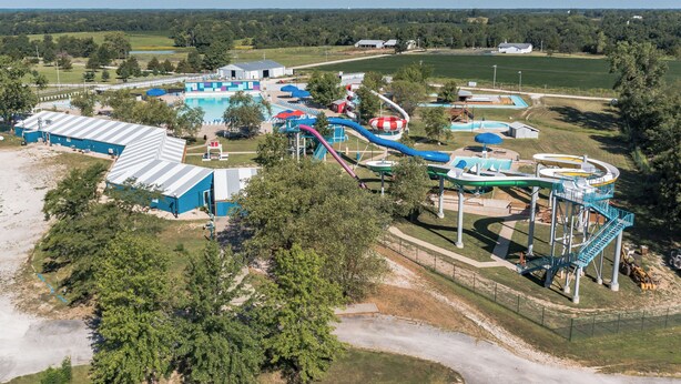 Une vue aérienne d’un parc aquatique doté de nombreux toboggans et de plusieurs piscines, entouré d’arbres et de vastes espaces verts.