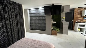 Een moderne slaapkamer met een bed, een televisie, een kitchenette en een groot raam met uitzicht.