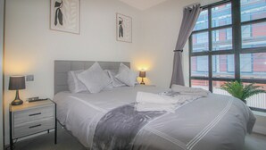 Ein ordentlich eingerichtetes Schlafzimmer mit einem Bett, Nachttischlampen und zwei gerahmten Bildern an der Wand.