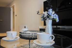 A dining area with a glass table, two white cups with saucers, a white vase with flowers, and a black and white patterned tray. - Birmingham Central|wifi|Parking|Sleeps 4 (Deritend)