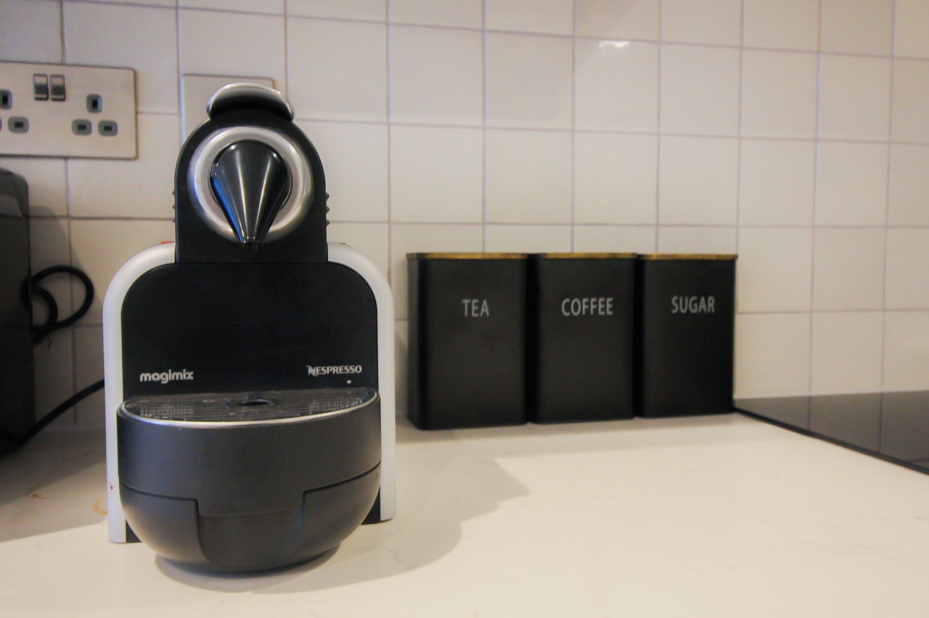 A Nespresso Magimix coffee machine on a kitchen counter with labeled containers for tea, coffee, and sugar.