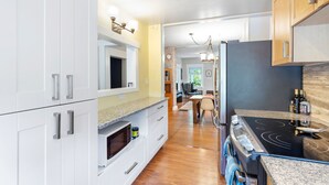 A modern kitchen with white cabinetry, a granite countertop, a black stove, and a dining area in the background. - Peaceful Kits Garden Stay (Vancouver)