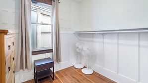 A room with a wooden floor, a window with curtains, a bench, and two standing fans. - Peaceful Kits Garden Stay (Vancouver)