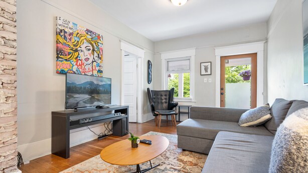A living room with a sofa, a coffee table, a TV, and a painting on the wall. - Peaceful Kits Garden Stay (Vancouver)