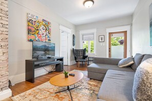 A living room with a sofa, a coffee table, a TV, and a painting on the wall. - Peaceful Kits Garden Stay (Vancouver)