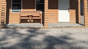 Een houten blokhut met twee verdiepingen, een balkon, een bank voor de deur en een garage.