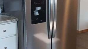 Een roestvrijstalen koelkast met een digitaal bedieningspaneel, in een keuken met houten vloeren en witte kasten.