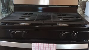 Een keuken met een roestvrijstalen fornuis, een magnetron erboven en een betegelde spatwand.
