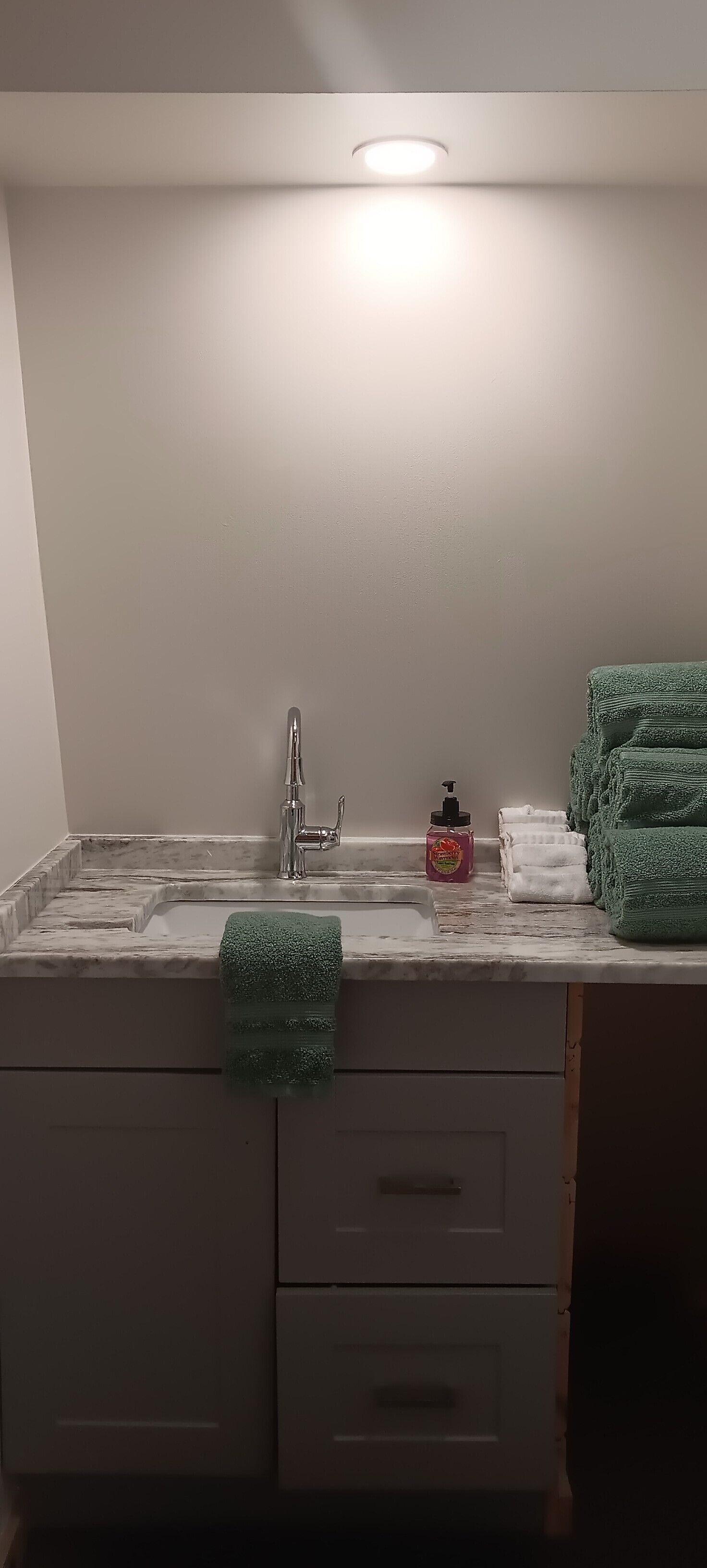 Une salle de bain avec un lavabo blanc, un miroir et une serviette verte accrochée au mur.