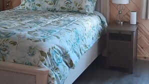 Een slaapkamer met een houten visgraat plafond, een bed met bloemenbeddengoed, twee bedlampen en een nachtkastje met een lamp.