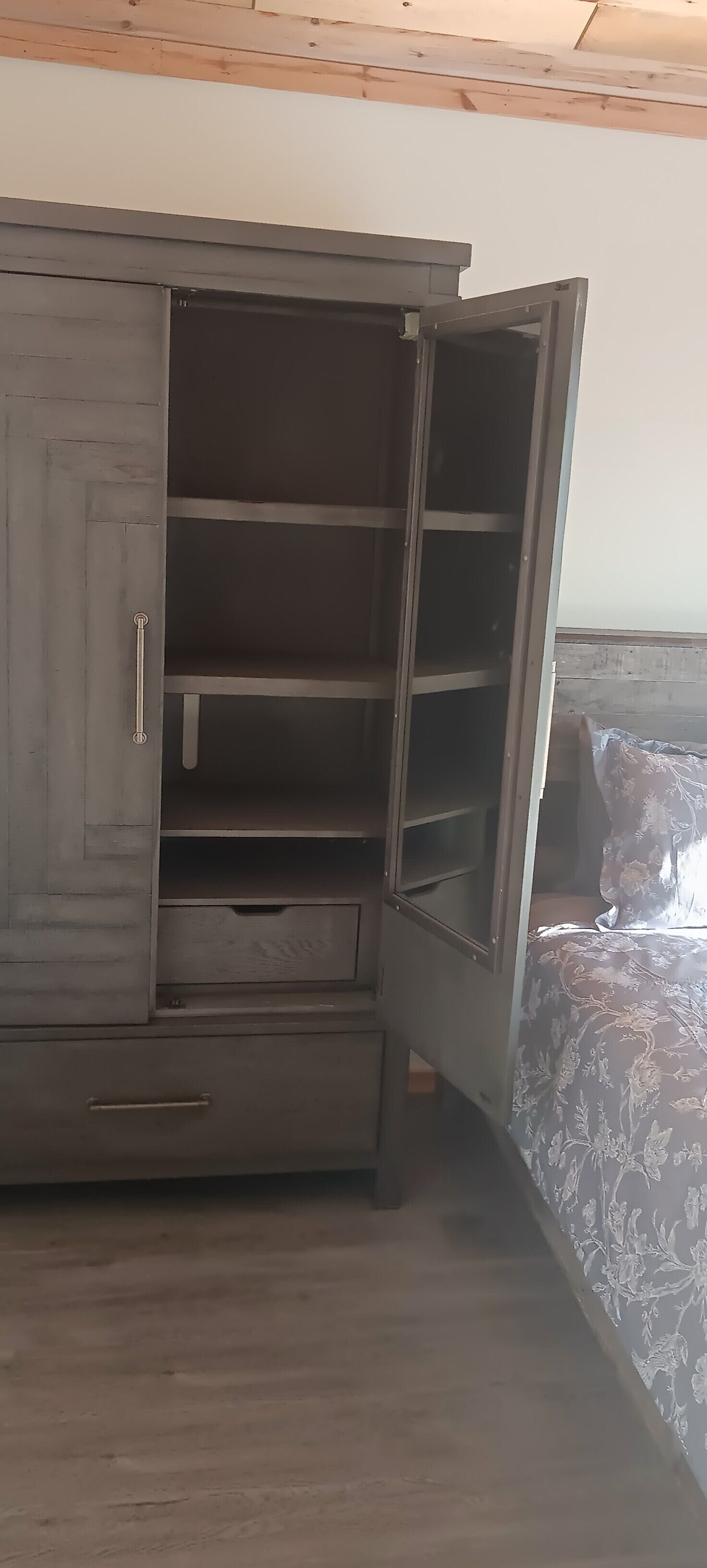 A room with a large wardrobe, a bed with floral bedding, and a wooden ceiling.