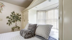 Un dormitorio con una cama grande, un espejo, una planta en maceta y una ventana con persianas.