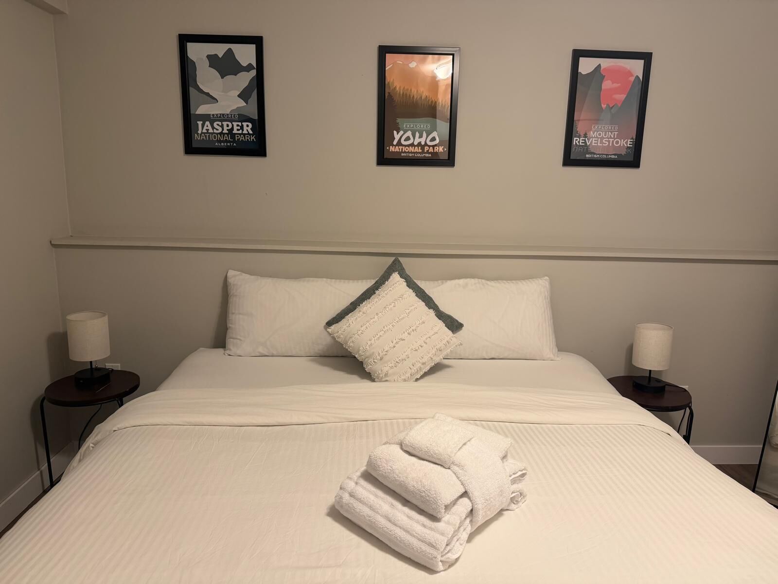 A hotel room with a bed, two bedside tables, and three framed posters on the wall.