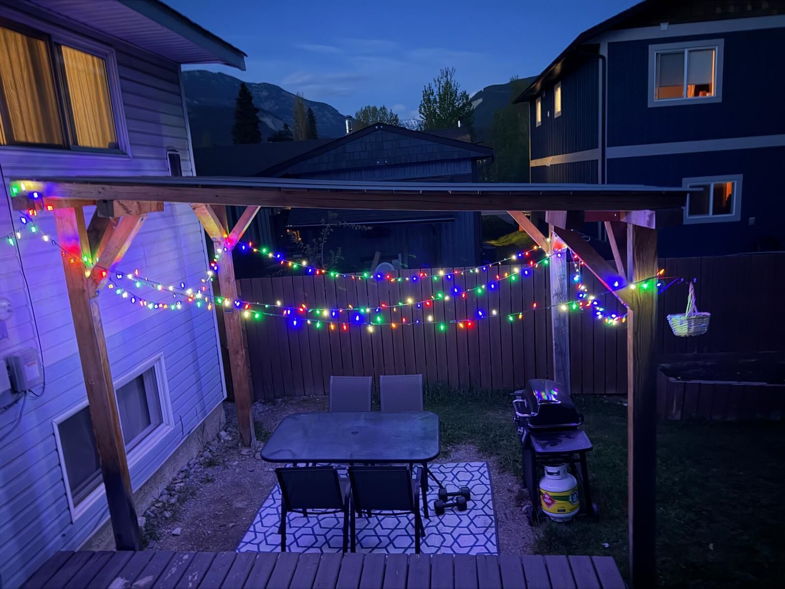 A backyard patio with a table and chairs, a grill, and a string of colorful lights.