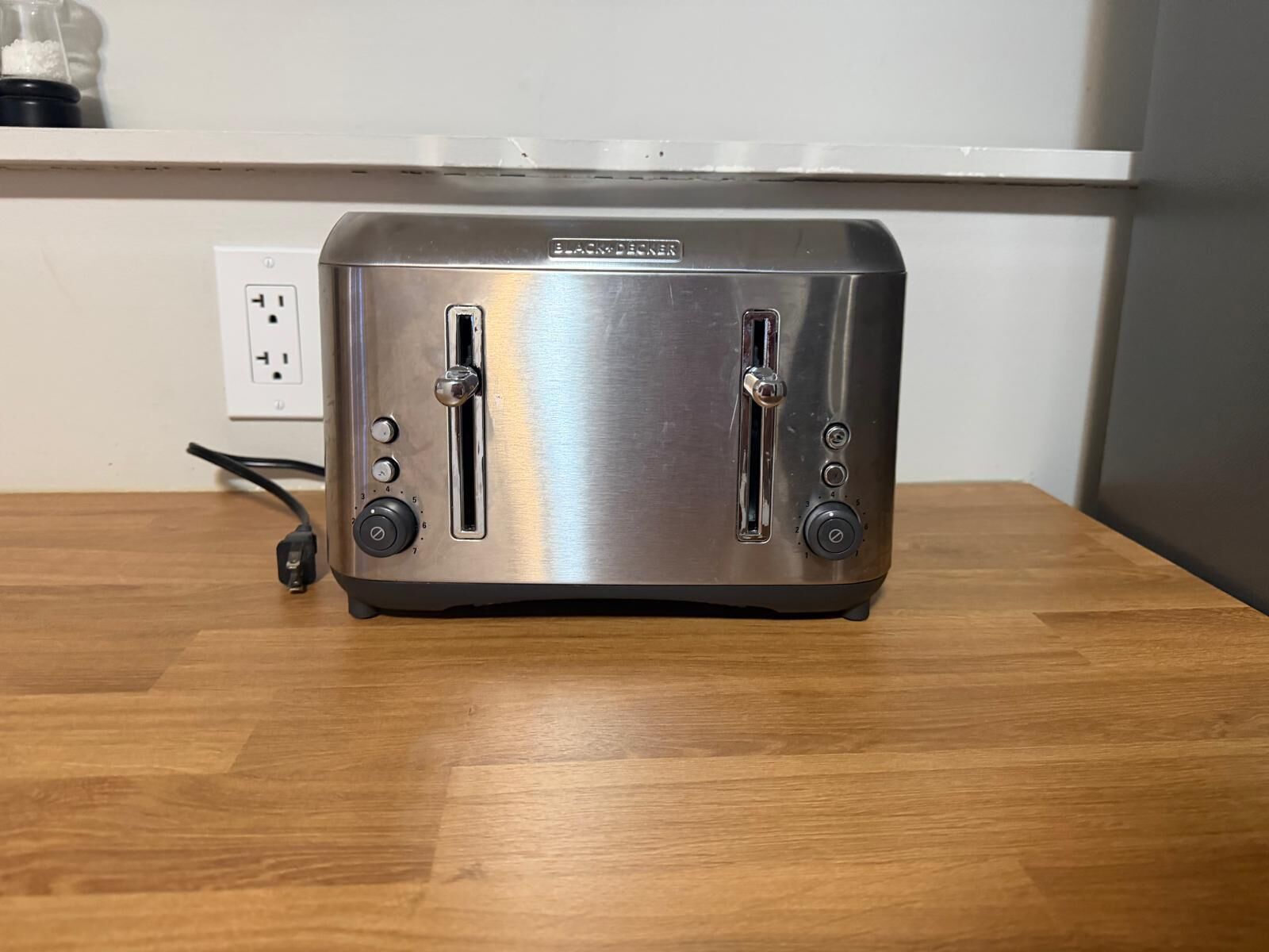 A stainless steel toaster on a wooden table with a power outlet and a cable in the background.