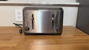 A stainless steel toaster on a wooden table with a power outlet and a cable in the background.