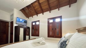Una camera da letto con un letto grande, travi a cassetto in legno, una televisione a parete e due finestre con persiane.