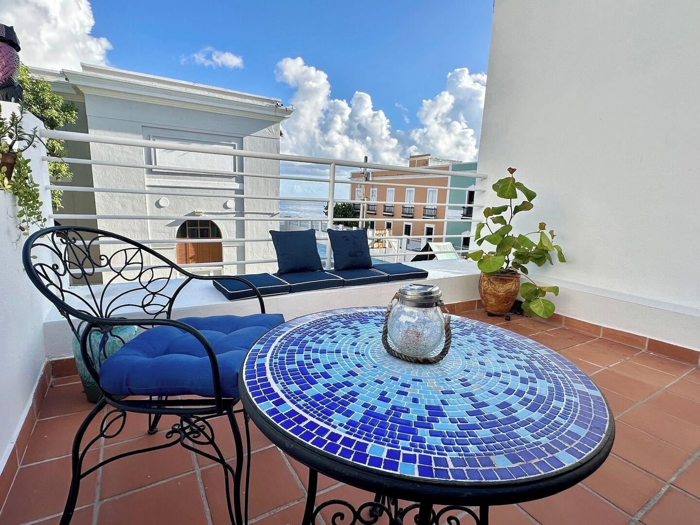A terrace with a round table, blue cushioned chairs, and a potted plant.