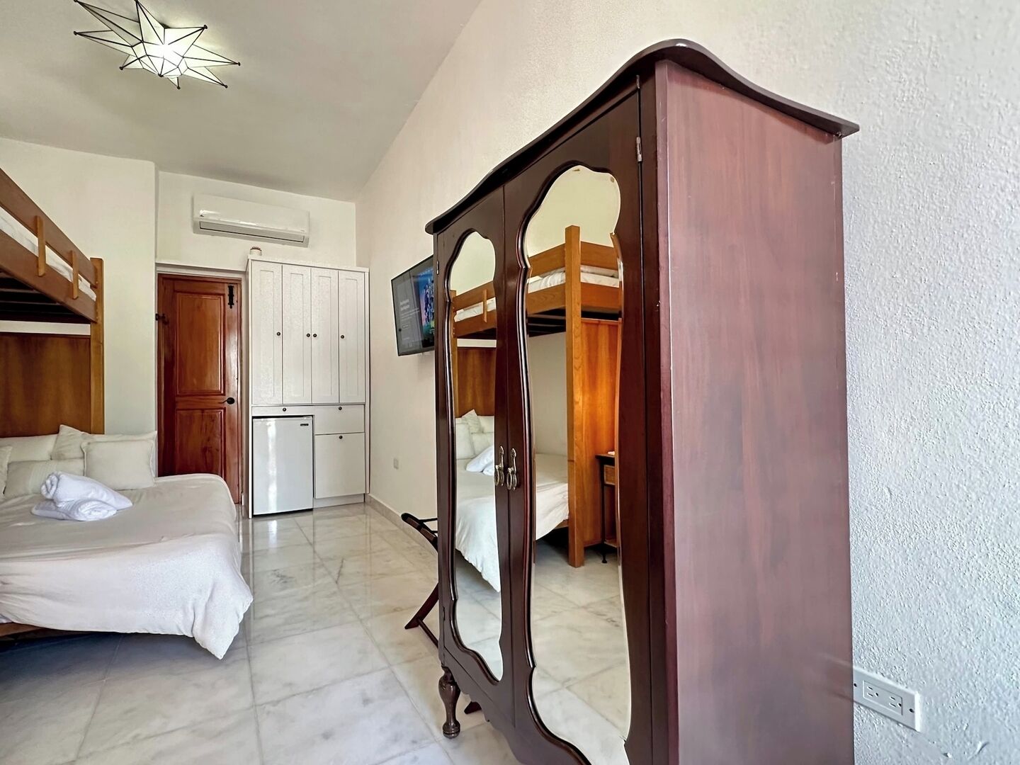 A room with a bunk bed, a wardrobe, a small kitchenette, and a mirror cabinet.