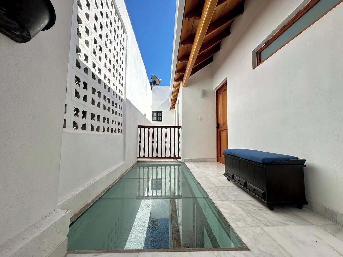 Un patio estrecho con suelo de vidrio, paredes blancas y techo de madera.
