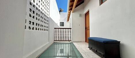A narrow courtyard with a glass floor, white walls, and a wooden ceiling.