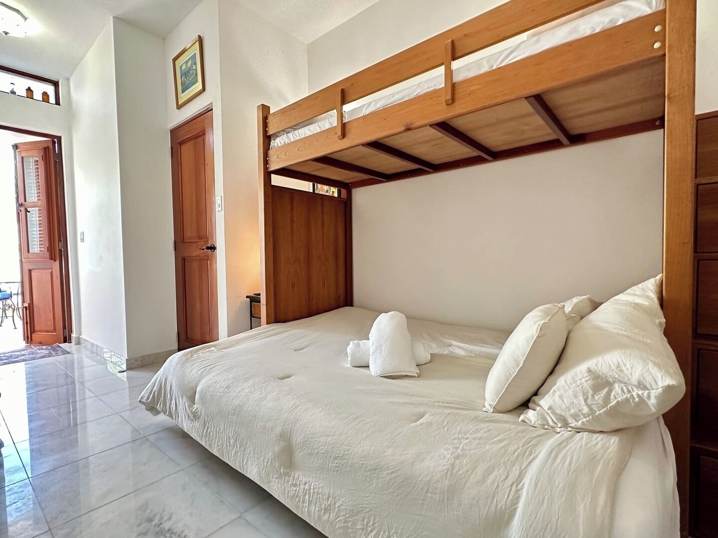 Un dormitorio con literas de madera, ropa de cama blanca y piso de baldosas.