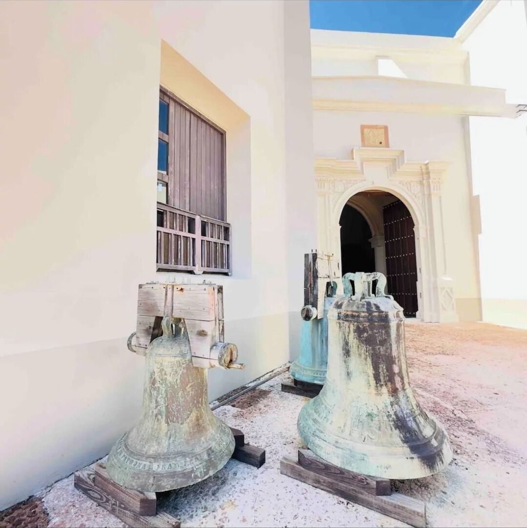 Two large, weathered metal sculptures in front of a white building with a window and an arched doorway.