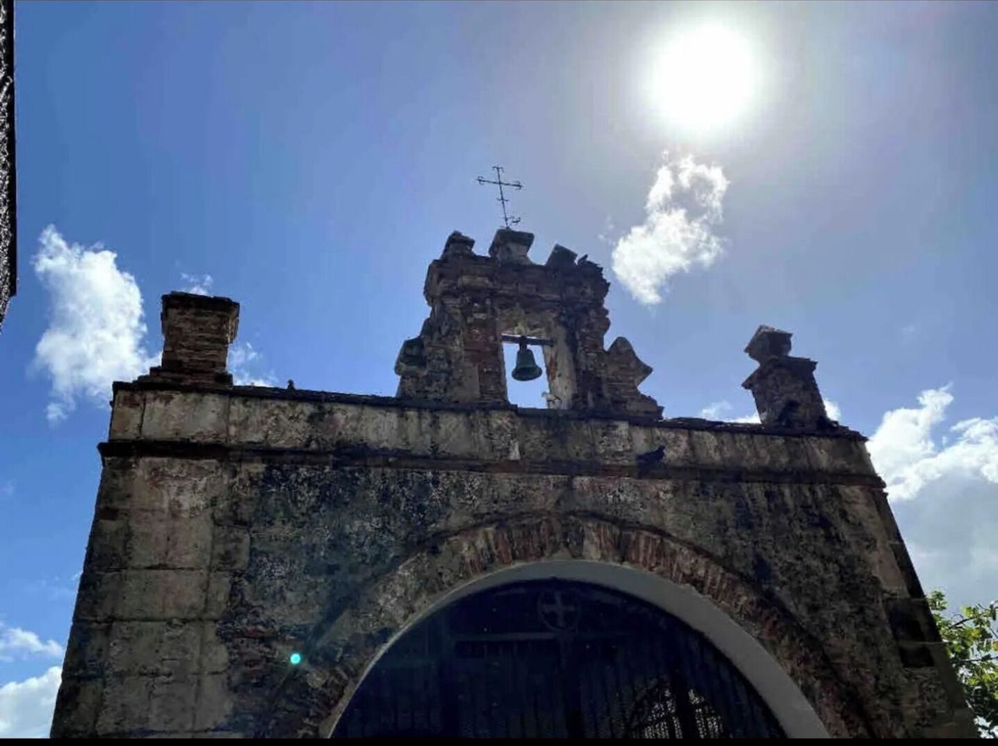 A historical stone archway with a bell tower and a cross on top.