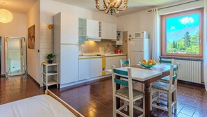 Une cuisine compacte avec des meubles blancs, une table à manger avec des chaises, un lustre et une fenêtre donnant sur les montagnes.